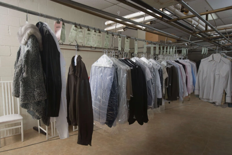 A variety of garments hanging on a conveyor system in a dry cleaning pickup and delivery facility, some are covered with plastic, Laundry Pickup Service Toronto