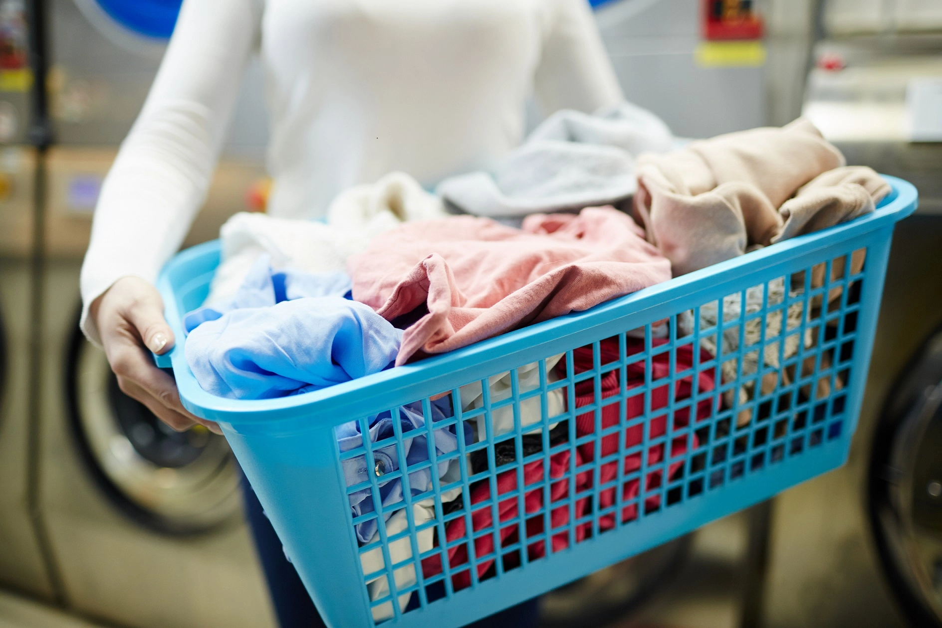 A person holding a blue laundry basket filled with clothes in an industrial washing service, linen services, Wash and Fold Laundry Service Toronto