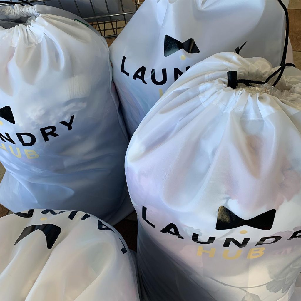 Four full laundry bags labeled "Laundry Hub," each featuring a bow tie design, neatly arranged on the floor.