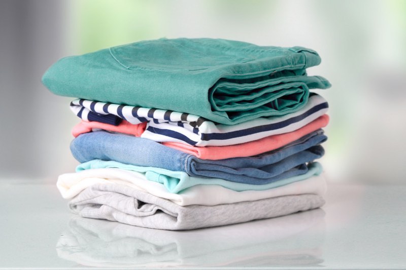 Stack of neatly folded clothes in various colors ready for wash and fold delivery on a table, Commercial Laundry Services Toronto