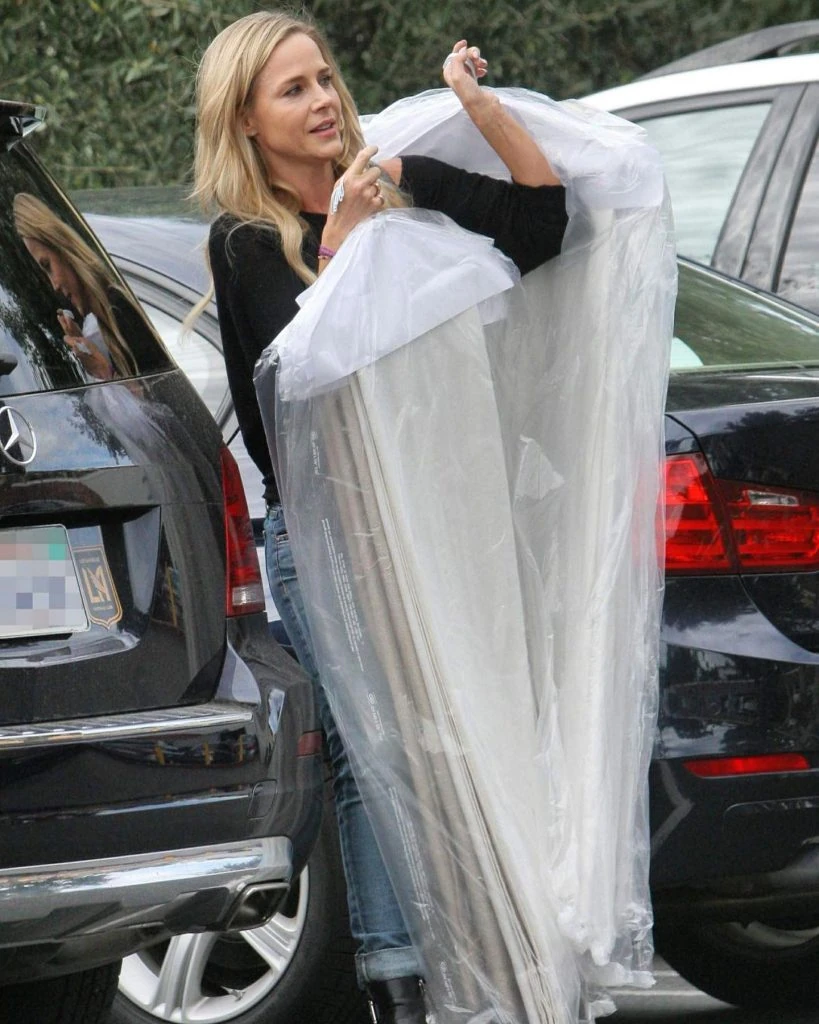 A woman in a black top unpacks a large plastic-wrapped item from the trunk of a Mercedes-Benz car, part of her laundry pickup and delivery service.