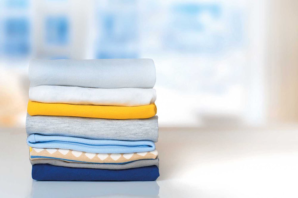 A stack of neatly folded clothes from a laundry service in various colors on a table, with a blurred light blue background.