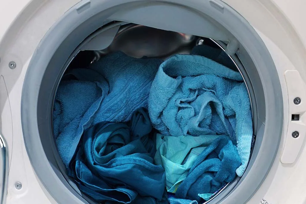 Open front-loading washing machine filled with blue towels, ideal for efficient laundry solutions.