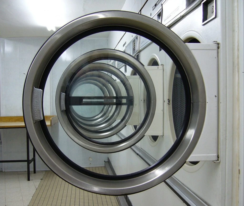 A row of open front-loading washing machines in a Pickering laundromat, viewed through the circular doors. A wooden counter and tiled floor add to the charm, while top-quality eco-friendly laundry solutions make it an ideal choice, Pickering with top-quality eco-friendly laundry solutions