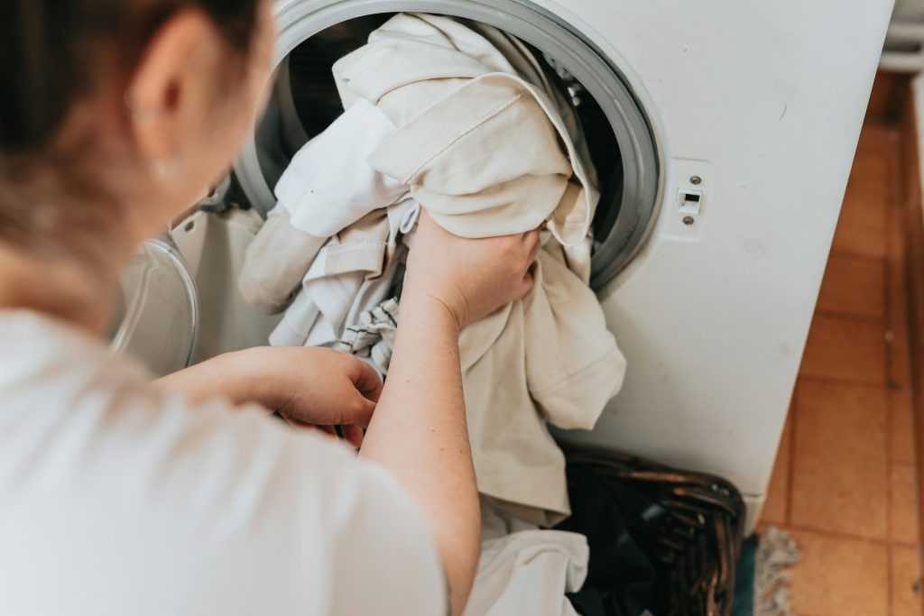 A person efficiently loads white laundry into a front-loading washing machine, showcasing the ease and convenience of on-demand laundry services in Oshawa.