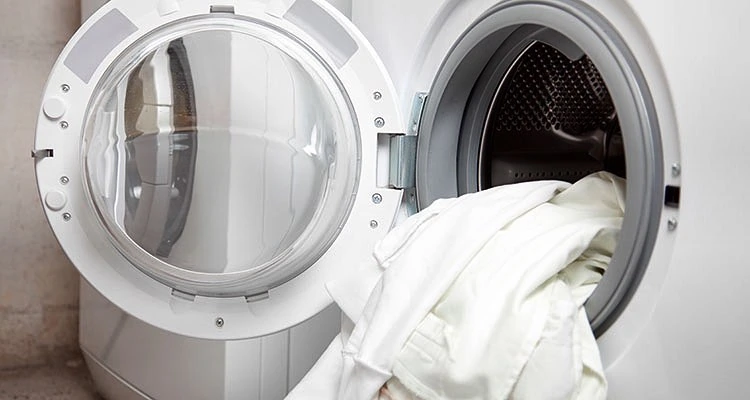 Front-loading washing machine with the door open, revealing white laundry inside, reminiscent of a professional laundry service's pristine results.